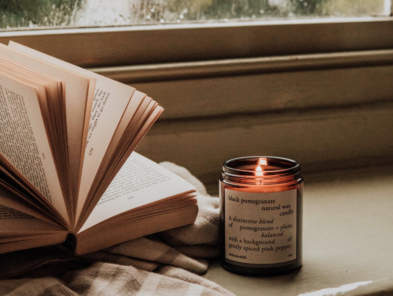black pomegranate candle sitting on a window sill with an open book